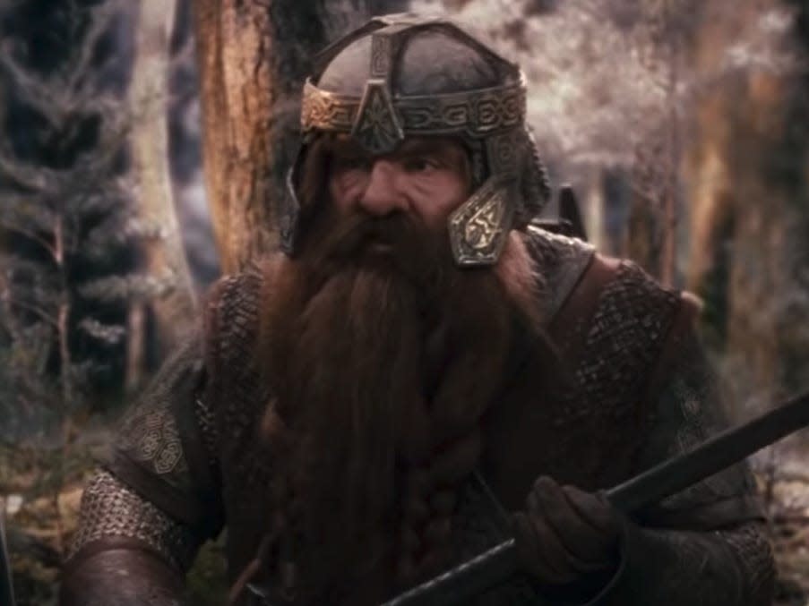 gimli wearing a bronze helmet and holding a spear in lord of the rings