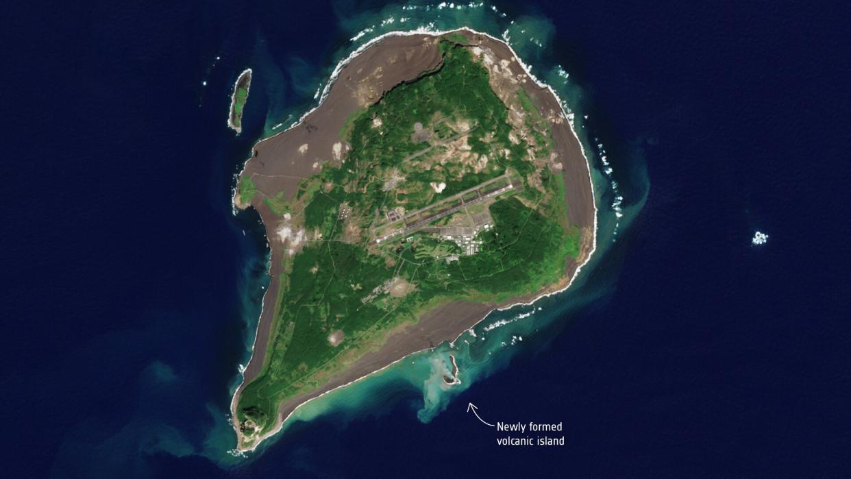  An overhead view of a green island surrounded by blue water. a much smaller island can be seen just below the larger island. 