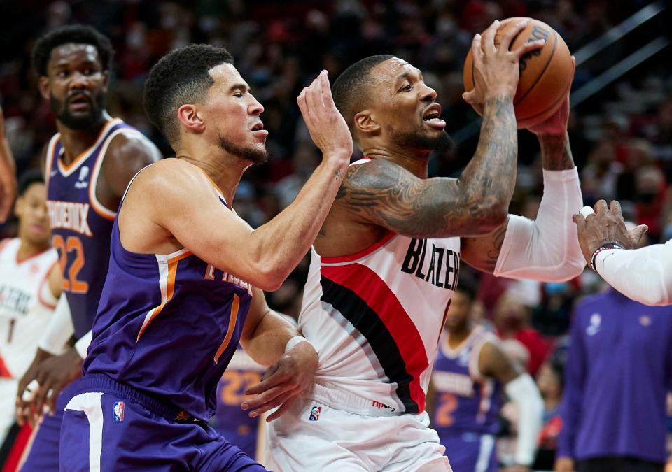 Portland Trail Blazers guard Damian Lillard (right) drives to the basket past Phoenix Suns guard Devin Booker during the first half of an NBA basketball game in Portland on Oct. 23, 2021.