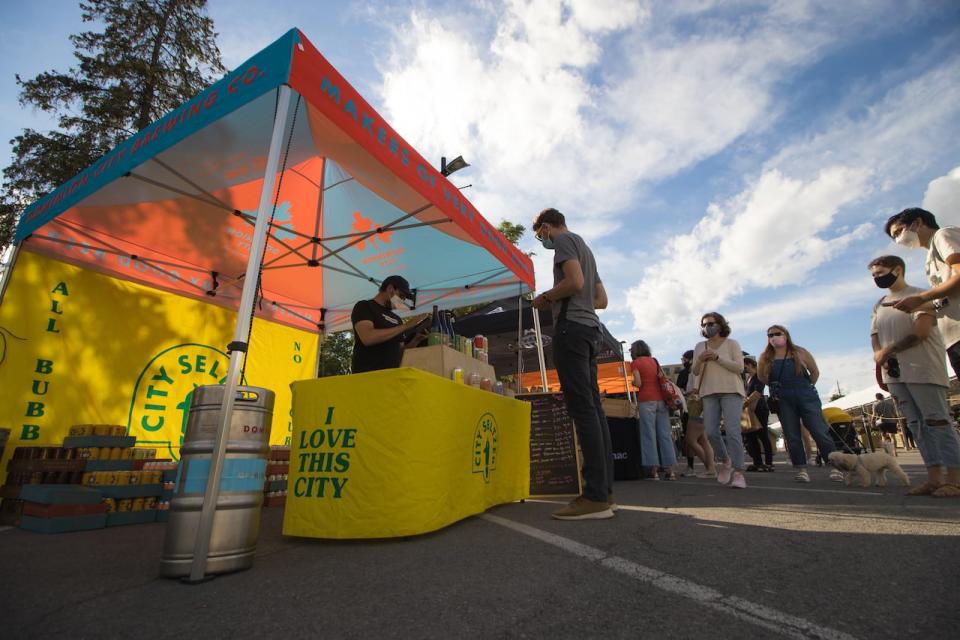 Josh McJannett of Dominion City Brewing, left, rings in a customer's purchase while people at the Parkdale Night Market wait in line on June 23, 2021.