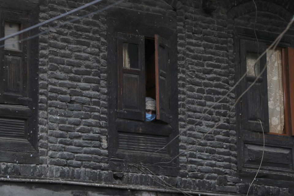 A Kashmiri woman wearing protective mask watches through a window of her house as an Indian policeman makes markings for people to maintain social distance at a market in Srinagar, Indian controlled Kashmir, Monday, April 6, 2020. (AP Photo/Mukhtar Khan)