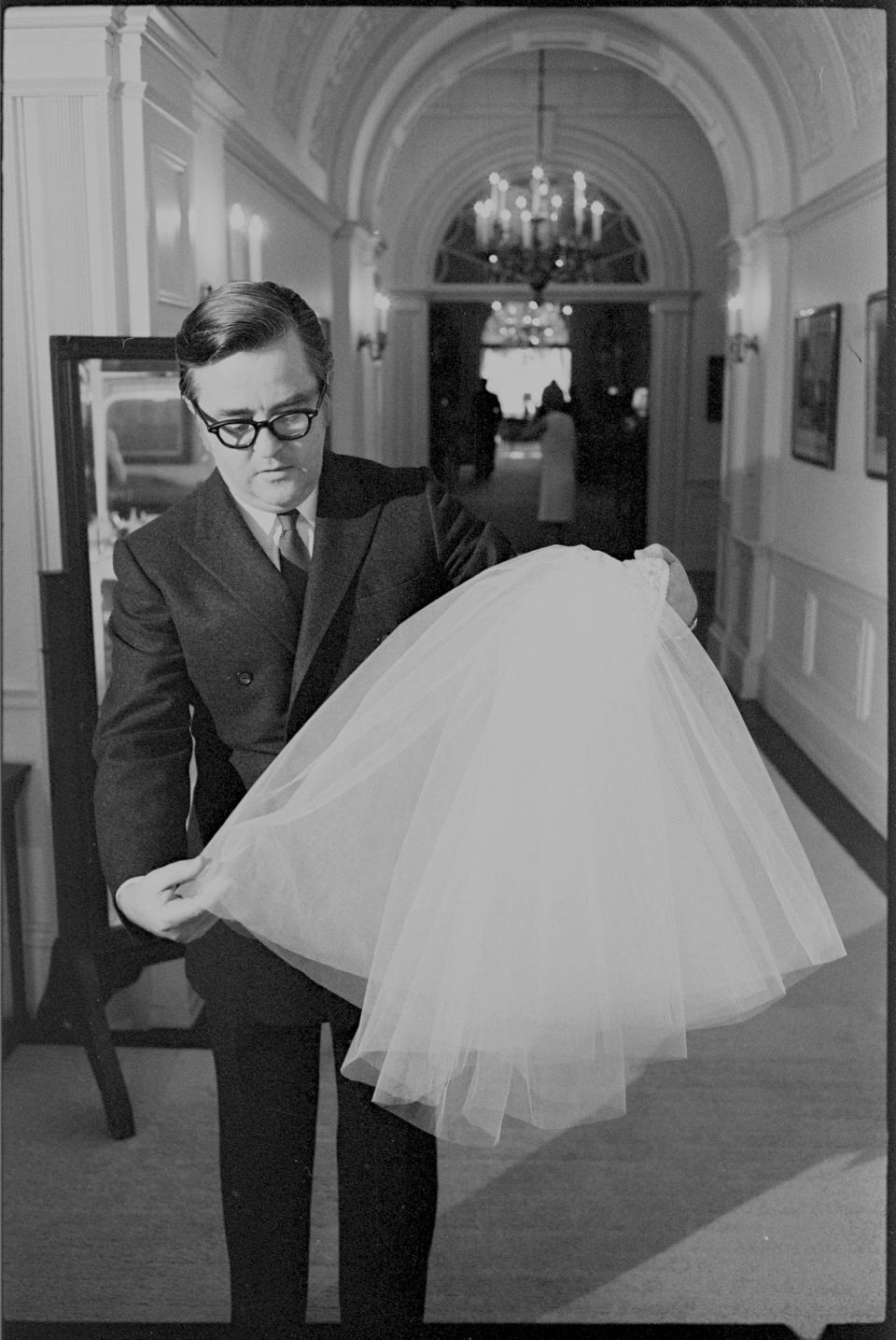 In this photograph by Yoichi R. Okamoto, designer Geoffrey Beene holds up the shoulder-length veil worn by Lynda Bird Johnson at her wedding on December 9, 1967. Beene was captured in the Center Hall on the Second Floor of the White House that day ahead of the wedding ceremony. Lynda Bird Johnson, daughter of President Lyndon B. Johnson and First Lady Lady Bird Johnson, married Marine Corps Capt. Charles S. Robb in the East Room. The veil was made of silk illusion and attached to a coronet made of the same silk satin fabric and embroidery as her gown.