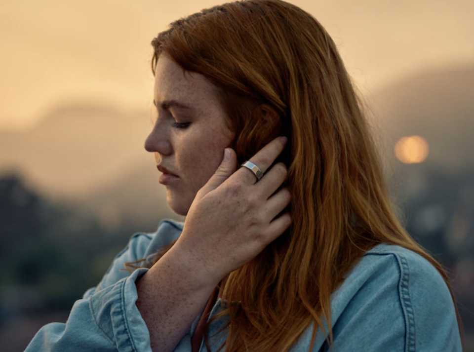 woman with long red hair wearing blue denim shirt and silver Oura Ring Gen3 (photo via Oura Ring)