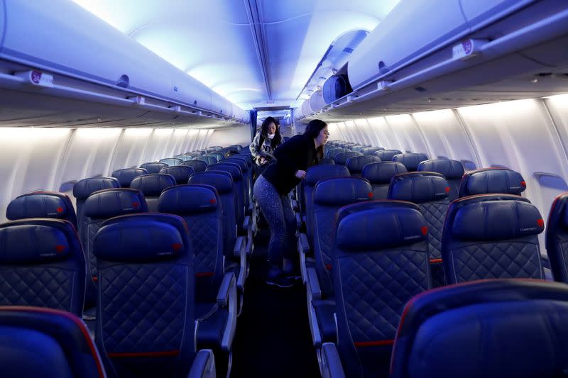 Air travelers grab carry-on luggage behind rows of empty seats aboard a Delta flight from New York to San Francisco