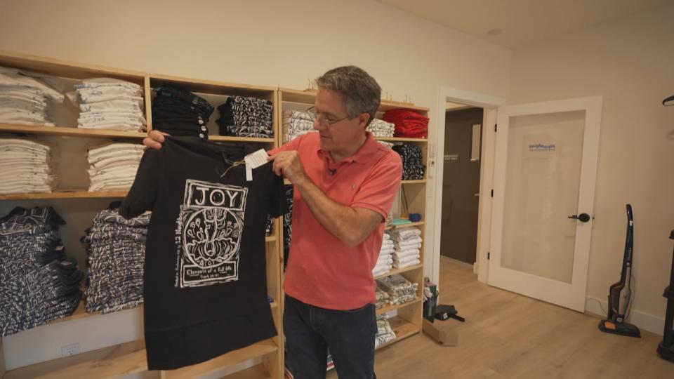 Marcel Lebrun, pictured here, started working on the 12 Neighbours tiny home community on Fredericton’s north side in 2021. Here, he holds up a t-shirt made through one of the community's other social enterprise projects. 