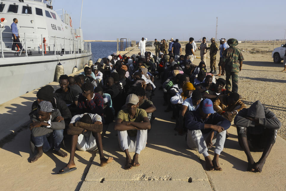 Rescued migrants are seated next to a coast guard boat in the city of Khoms, around 120 kilometers (75 miles) east of Tripoli, Libya, Tuesday, Oct. 1, 2019. (AP Photo/Hazem Ahmed)