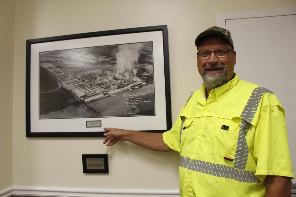 Mike Collins has worked at the Savannah Mill for 42 years. He comes from a generation of mill workers. Collins is pointing to a 1944 rendering of the plant. (International Paper 85th anniversary 2021).