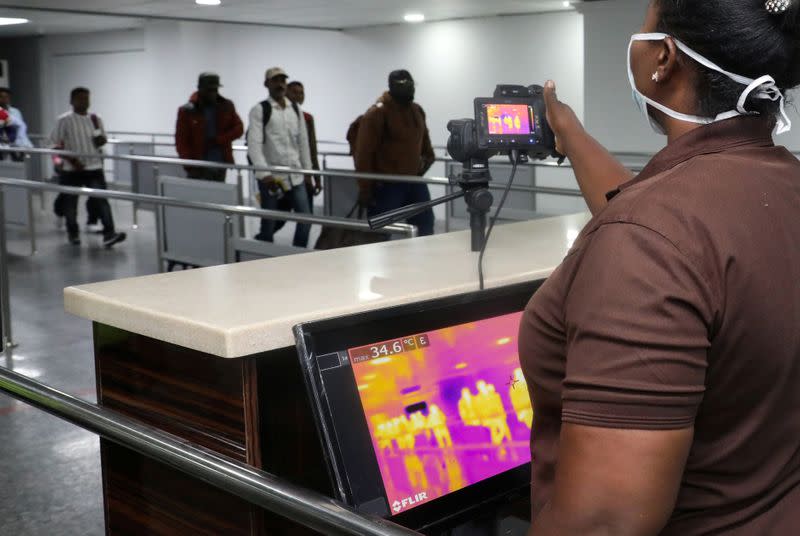 Officials monitor thermal scanners as passengers walk past upon arrival of a flight to Lagos