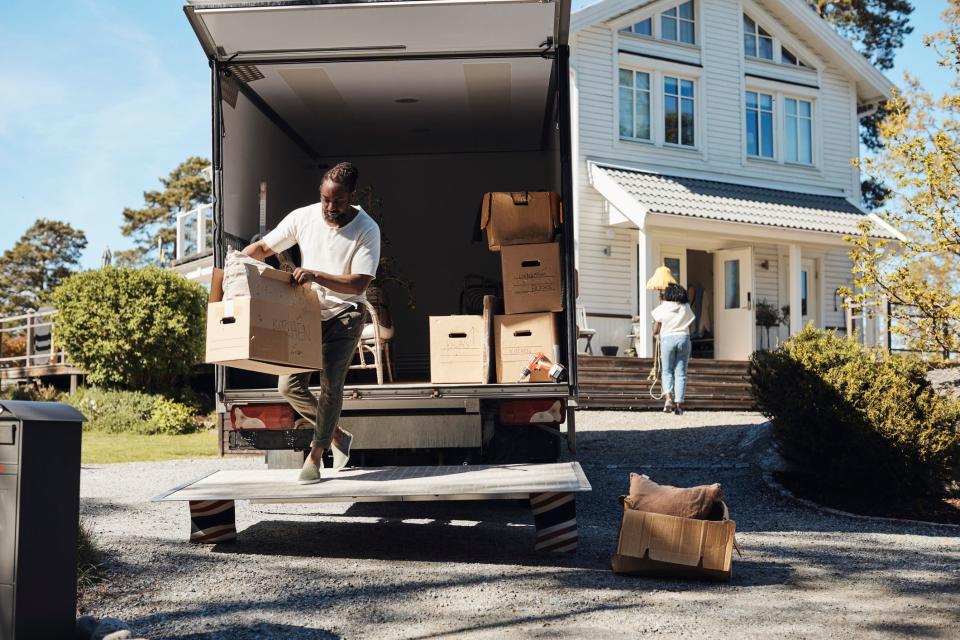 A couple moving boxes from a van into a house.