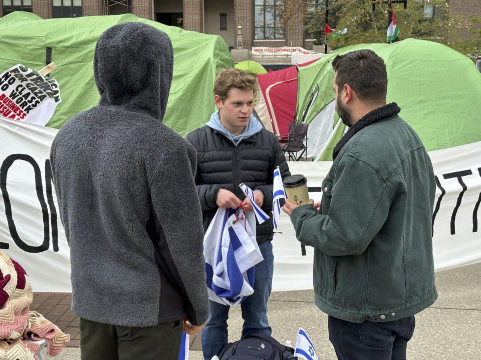 University of Michigan computer science junior Josh Brown, center, hands out miniature blue and white flags of Israel while standing Wednesday, April 23, 2024, in front of a banner reading “LONG LIVE THE INTIFADA," in Ann Arbor, Mich. The banner is part of a protest by students and groups demanding the Ann Arbor school divest from companies that do business with Israel. (AP Photo/Corey Williams)