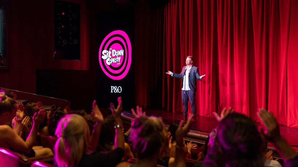 A man performs comedy on stage on a P&O comedy cruise.