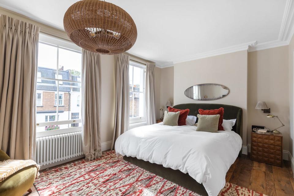 an image of the property's principal bedroom featuring a large rattan light fixture, double windows, fully styled bed, oval mirror and art deco nightstand