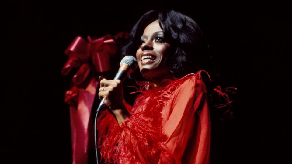 diana ross sings while holding a microphone, she wears a red glamorous gown