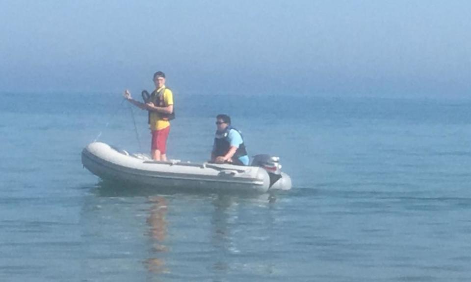 A couple of officials in a dinghy warn people to get out of the water.