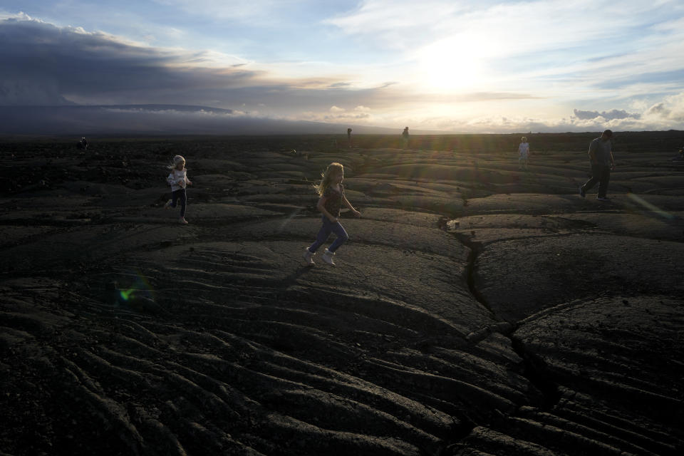 Children run on blackened lava rock from a previous eruption near the Mauna Loa volcano as it erupts Wednesday, Nov. 30, 2022, near Hilo, Hawaii. (AP Photo/Gregory Bull)