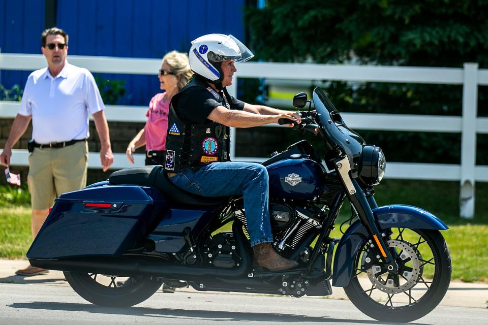 mike pence rides a harley motorcycle wearing a helmet, blue jeans, cowboy boots, and a leather vest with patches on it