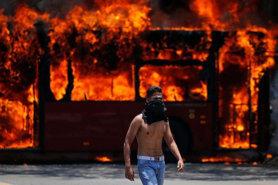 An anti-government protester walks near a bus that was set on fire by opponents of Venezuela's President Nicolas Maduro during clashes between rebel and loyalist soldiers in Caracas, Venezuela, Tuesday, April 30, 2019. Venezuelan opposition leader Juan GuaidÃ³ took to the streets with a small contingent of heavily armed troops early Tuesday in a bold and risky call for the military to rise up and oust Maduro. (AP Photo/Fernando Llano)