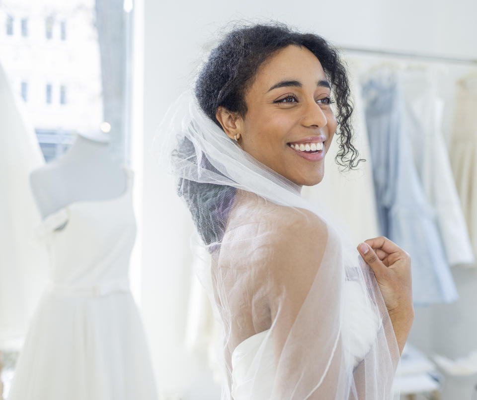 A bride smiles brightly while trying on a wedding dress and veil in a bridal shop