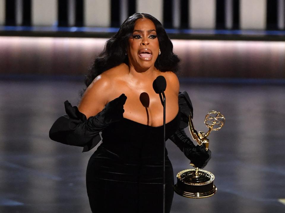 niecy nash-betts accepts the award for outstanding supporting actress in alimited series at the emmys. she's holding the statue in her left hand and pointing at herself with her right, speaking into the microphone