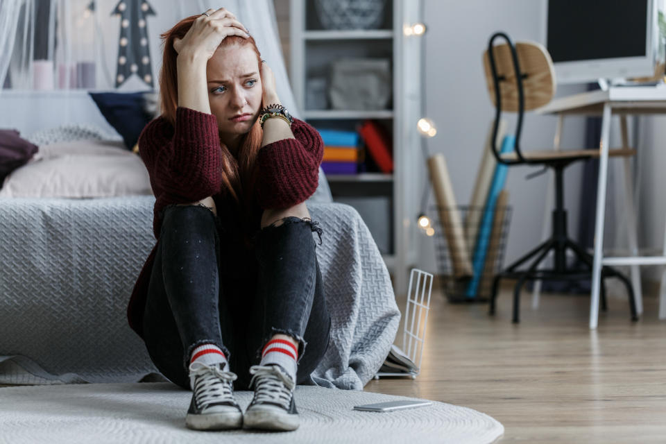 Adult in a sweater and jeans sits on the floor looking worried, with a child's room in the background