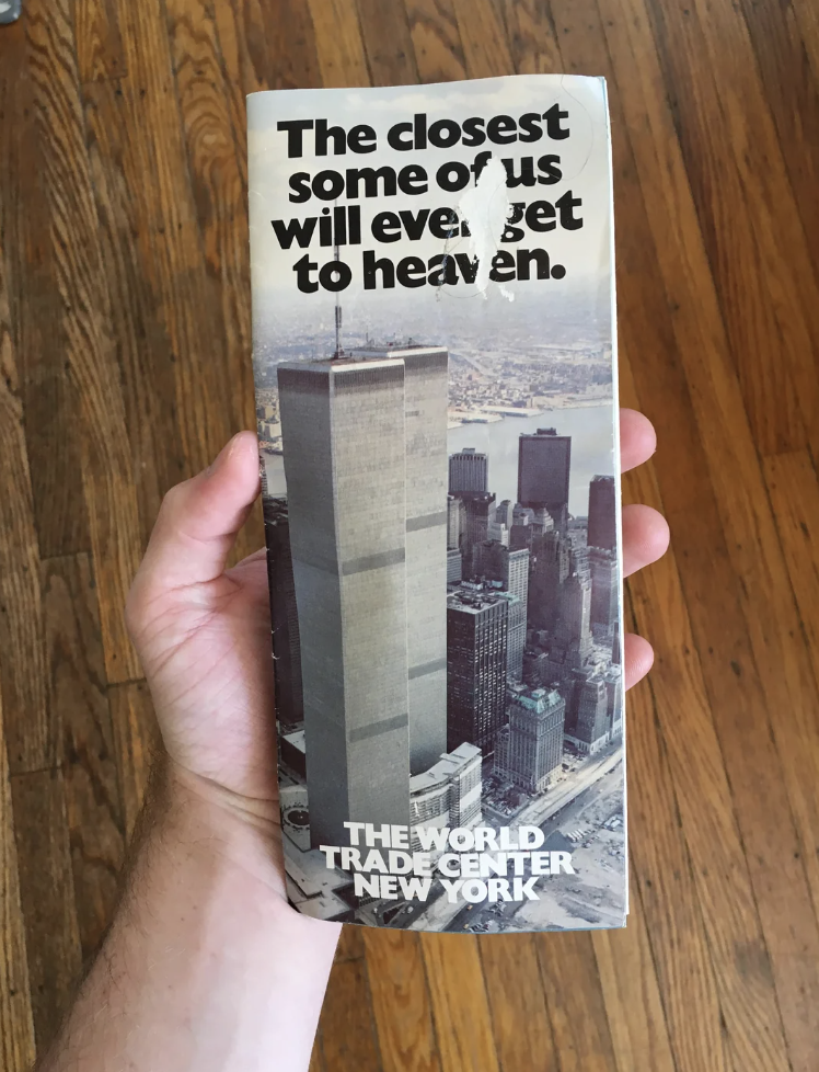 Hand holding a brochure with an image of the Twin Towers captioned, "The closest some of us will ever get to heaven. THE WORLD TRADE CENTER NEW YORK"