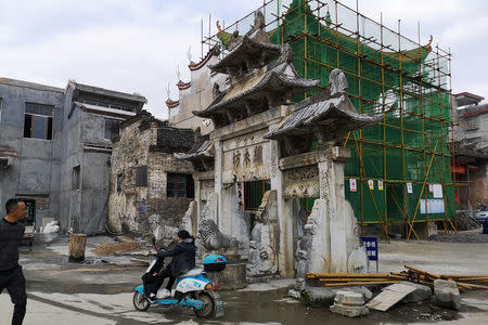 A woman rides a motorcycle past an imperial-style arch and a building under renovation in Rucheng county, Hunan province, China December 3, 2018. Picture taken December 3, 2018. REUTERS/Shu Zhang