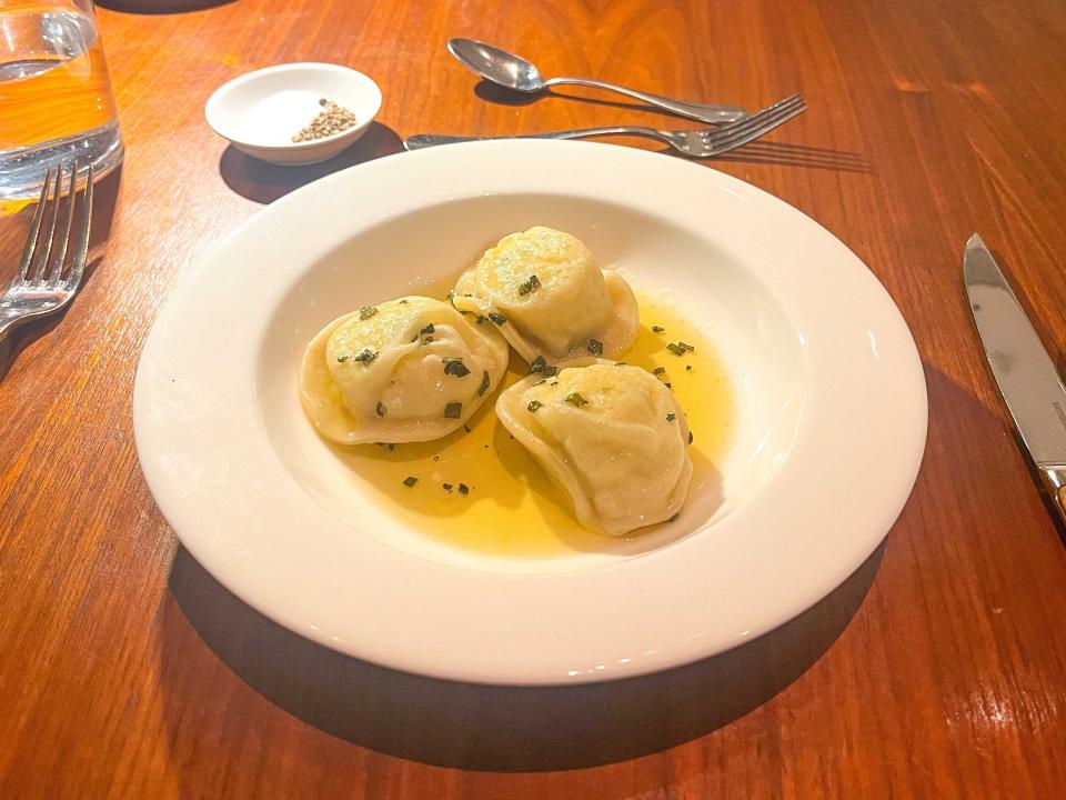 A white bowl holding three pierogi with herbs and a yellow sauce on top