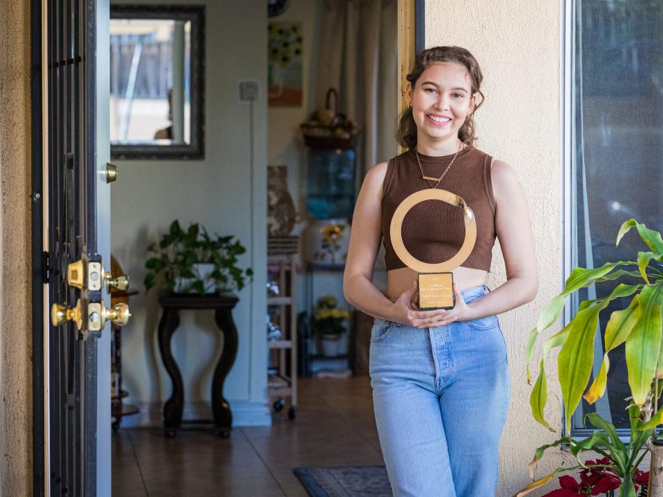Nalleli Cobo holds circular Goldman Environmental Prize with plaque posing in front of home