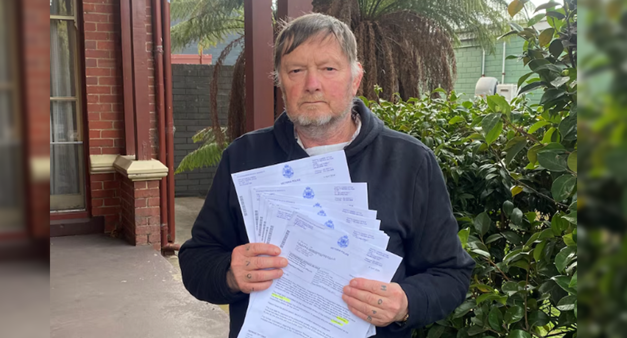 Kelvin Bennett stands holding some of the driving infringements he has received. 