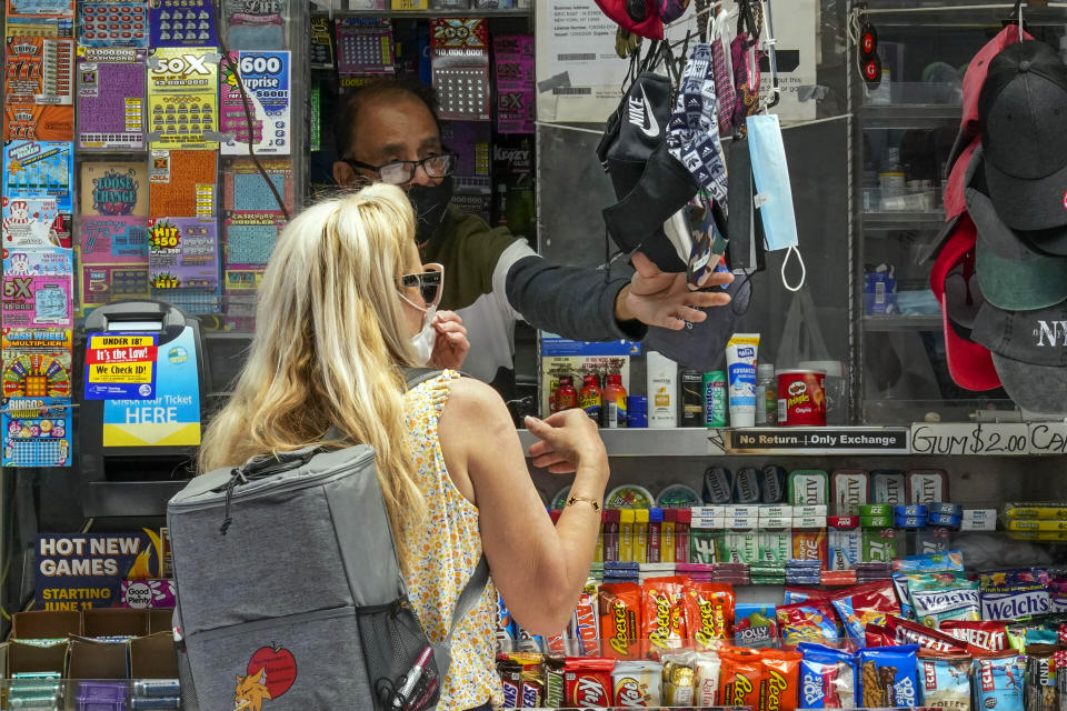 FILE — In this May 17, 2021 file photo, a woman buys a face mask at a newspaper stand in the East Village of New York. New York Gov. Andrew Cuomo and New York City Mayor Bill de Blasio have scheduled competing news conferences Monday, Aug. 2 amid rising COVID-19 case counts attributed to the highly contagious delta variant of the virus. (AP Photo/Mary Altaffer)
