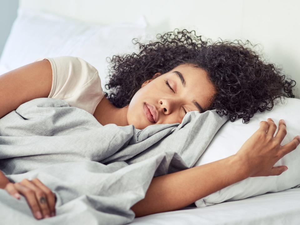 A young woman with curly hair sleeping peacefully in bed in a sunlit room.