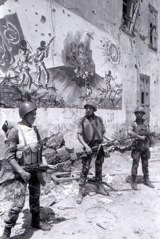 Syrian soldiers carry their weapons as they stand in front of a damaged building, in Beirut