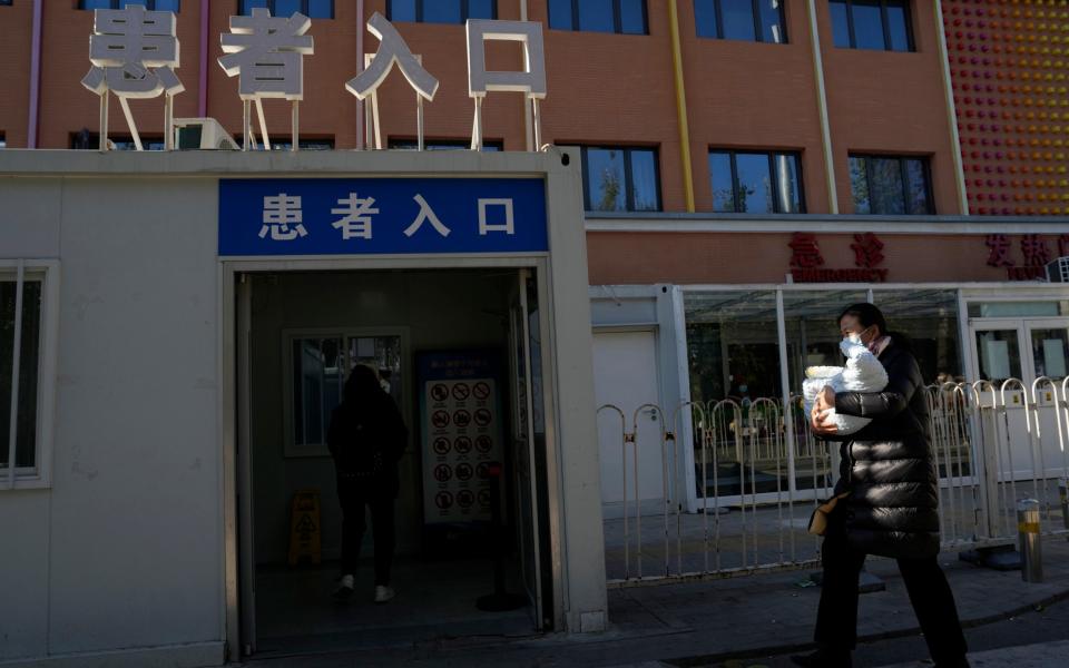 A visitor carries a child into the children's hospital with a sign "Patient entrance" in Beijing, Friday, Nov. 24, 2023