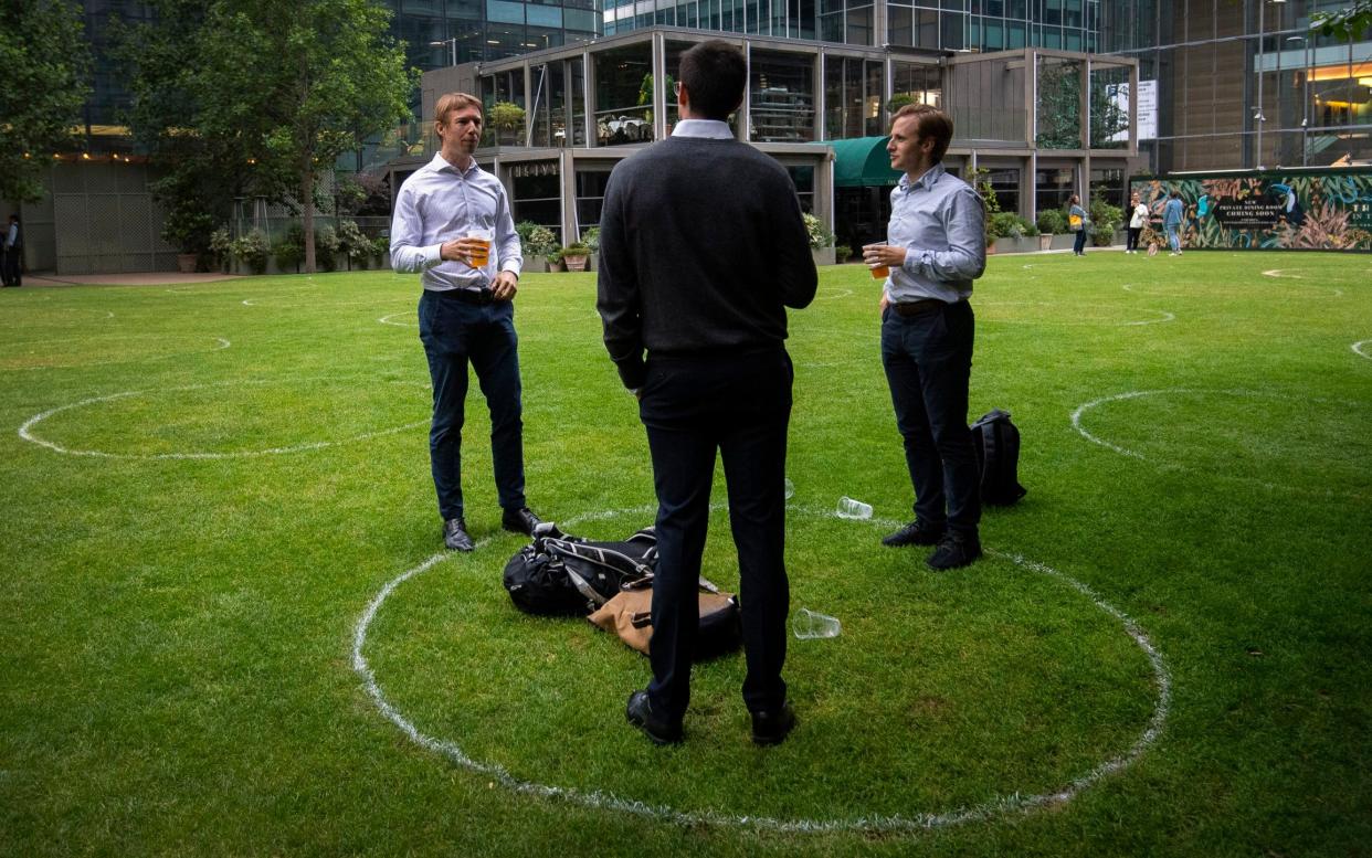 Drinkers stand within rings marked on the grass to maintain their social distance outside a bar in Canary Wharf, East London as further coronavirus lockdown restrictions are lifted in England - PA