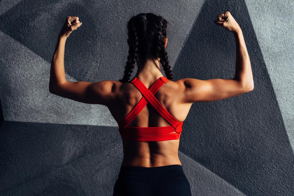 back view portrait of a woman flexing her back and shoulder muscles, wearing a strappy red sports bra