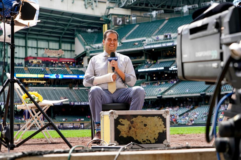 Los Angeles Dodgers television reporter David Vassegh works on a pregame broadcast before a baseball game against the Milwaukee Brewers Thursday, Aug. 18, 2022, in Milwaukee. Vassegh said he broke two bones in his right wrist and cracked six ribs Wednesday when he tumbled and crashed into the padding at the end of his slide down "Bernie's Chalet," where Brewers mascot Bernie Brewer takes up residence behind the American Family Field left-field stands. (AP Photo/Morry Gash)