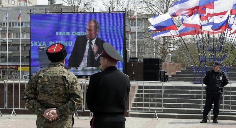Cossacks look at Russian President Vladimir Putin answering a question during his annual televised phone-in with the nation on an outdoor screen, in Simferopol on April 16, 2015