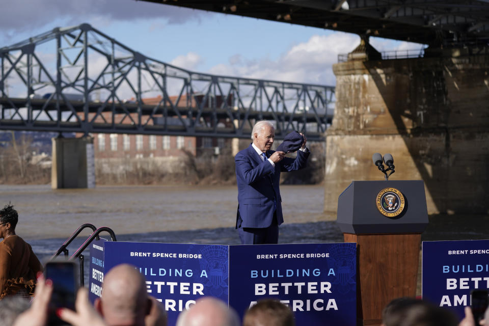 President Joe Biden puts on a hat as he arrives to speak about his infrastructure agenda under the Clay Wade Bailey Bridge, Wednesday, Jan. 4, 2023, in Covington, Ky. Biden's infrastructure deal that was enacted in late 2021 will offer federal grants to Ohio and Kentucky to build a companion bridge that is intended to alleviate traffic on the Brent Spence Bridge, in background at left. (AP Photo/Patrick Semansky)