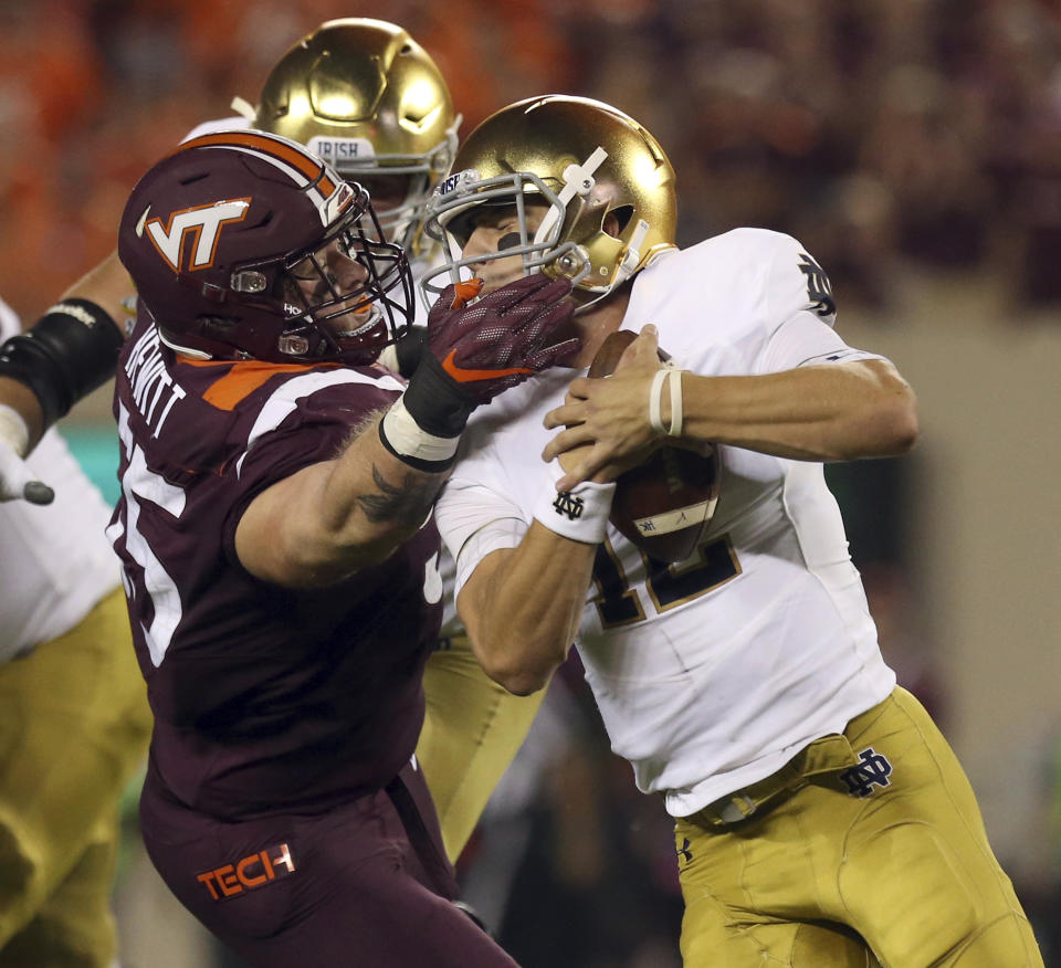 Virginia Tech's Jarrod Hewitt (55) grabs Notre Dame quarterback Ian Book (12) by the face mask and is called for a personal foul during the first quarter of an NCAA college football game Saturday, Oct. 6, 2018, in Blacksburg, Va. (Matt Gentry/The Roanoke Times via AP)