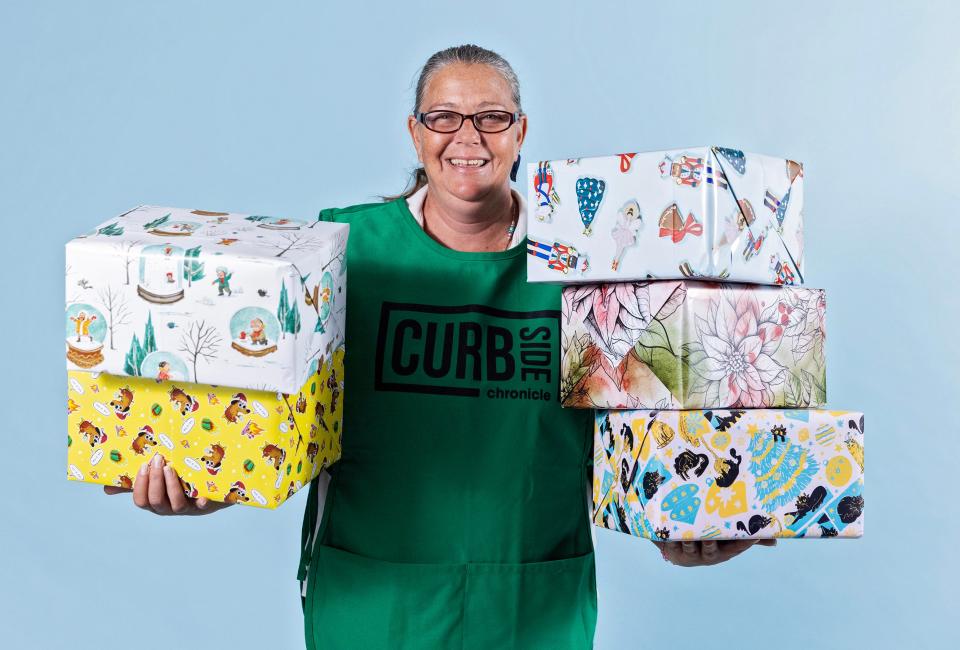 Curbside Chronicle vendor Rebecca holds packages wrapped in paper available through the OKC street paper's 2023 Wrap Up Homelessness program. All proceeds from wrapping paper sales support the Curbside Chronicle and its mission to employ and empower people transitioning out of homelessness in OKC.