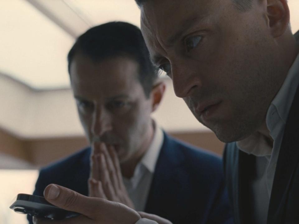 A close up of two white men hovering over a cell phone and looking concerned.