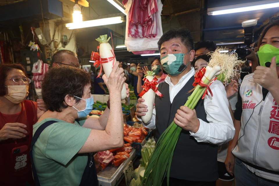 民進黨台北市長參選人陳時中（前右）5日在北投市場掃街拜票，攤商送上蘿蔔象徵好彩頭。（中央社）