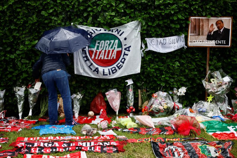 Una persona deja una carta entre flores y recuerdos de fútbol cerca de Villa San Martino, la residencia del ex primer ministro italiano Silvio Berlusconi, a la que fue trasladado su cuerpo tras su muerte, en Arcore, cerca de Milán, Italia