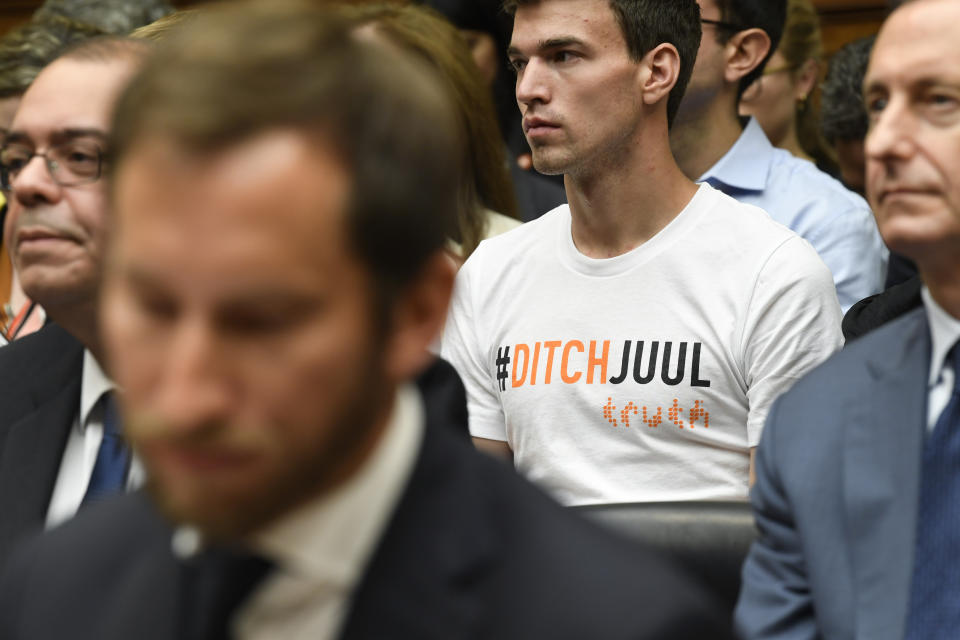 A person in the audience wears a shirt against JUUL as JUUL Labs co-founder and Chief Product Officer James Monsees, foreground, testifies before a House Oversight and Government Reform subcommittee on Capitol Hill in Washington, Thursday, July 25, 2019, during a hearing on the youth nicotine epidemic. (AP Photo/Susan Walsh)