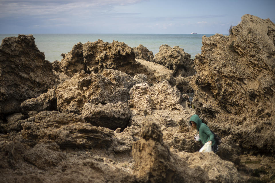 A woman cleans rocks covered in tar from an oil spill in the Mediterranean sea in Gador nature reserve near Hadera, Israel, Saturday, Feb. 20, 2021. Hundreds of volunteers are taking part in a cleanup operation of Israeli shoreline as investigations are underway to determine the cause of an oil spill that threatens the beach and wildlife, at Gador Nature Reserve near the northern city of Hadera, the tar smeared fish, turtles, and other sea creatures. (AP Photo/Ariel Schalit)
