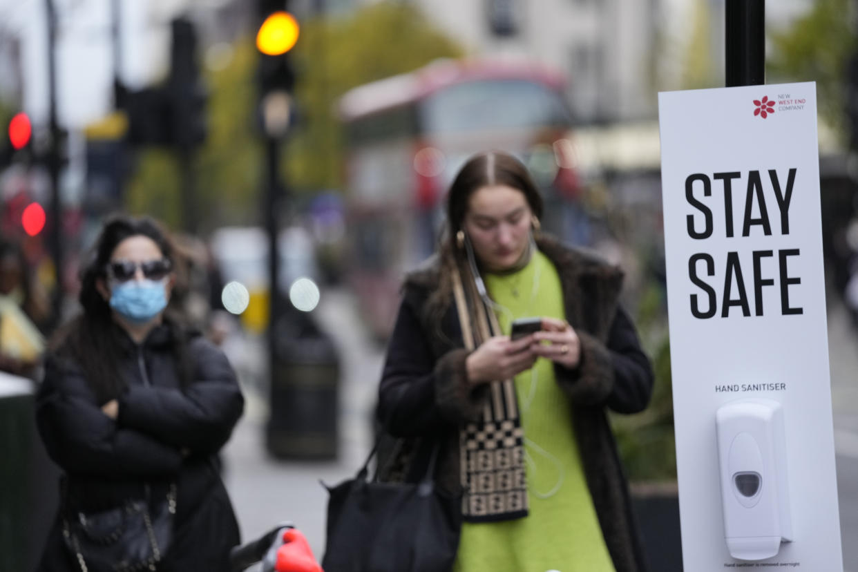 Bus passengers wait at a bus stop next to a Stay Safe sign which encourages social distancing and the wearing of masks to curb the spread of COVID-19, in London, Tuesday, Nov. 30, 2021. The emergence of the new COVID-19 omicron variant and the world's desperate and likely futile attempts to keep it at bay are reminders of what scientists have warned for months: The coronavirus will thrive as long as vast parts of the world lack vaccines.(AP Photo/Alastair Grant)