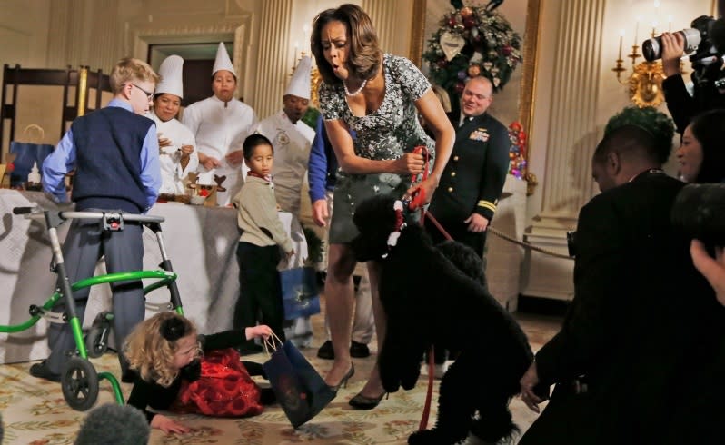 First Lady Michelle Obama reacts as Ashtyn Gardner, 2, loses her balance when she was greeting Sunny, one of the presidential dogs, as children of military families participate in a holiday arts and crafts event in the State Dining Room at the White House in Washington. Picture: AP