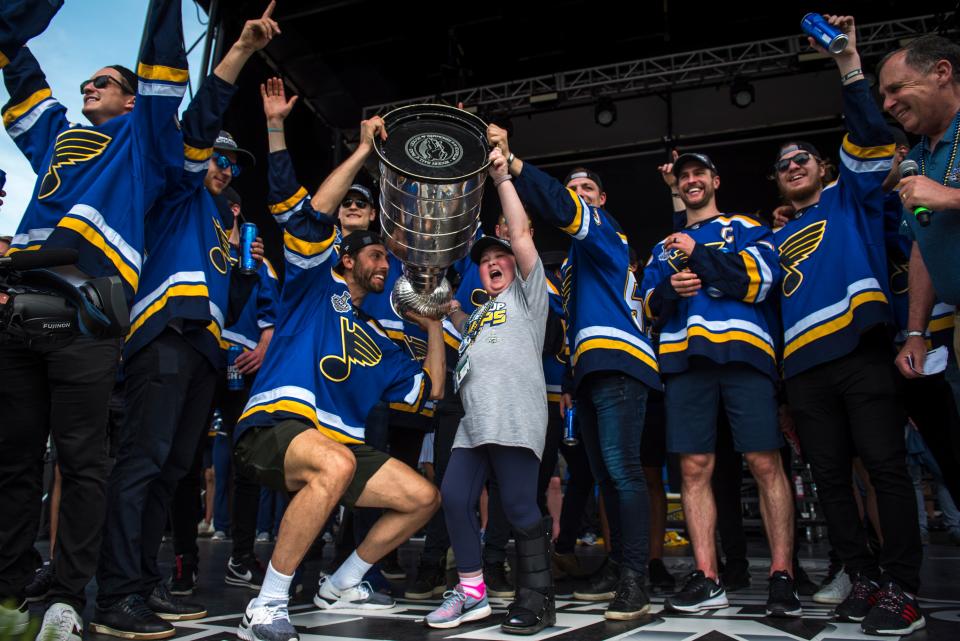 Colton Parayko and other Blues players help superfan Laila Anderson hoist the Stanley Cup.