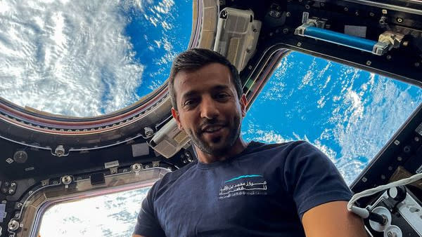  a man floats in front on windows in space. The Earth is visible 