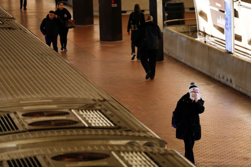 FILE PHOTO: A morning commuter holds a towel covering a face after departing from a Metro train car, as Mayor Muriel Bowser declared a State of Emergency due to the coronavirus disease (COVID-19), inside the Metro Center underground subway station, in Wash